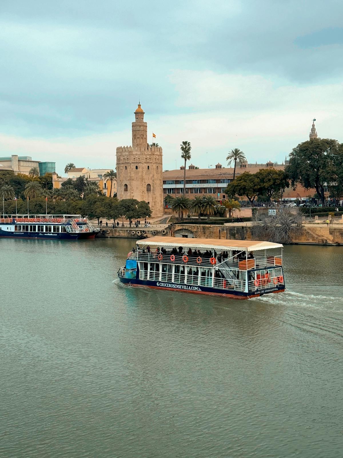 Cruise boat on the Guadalquivir River passing the Torre del Oro in Seville Spain