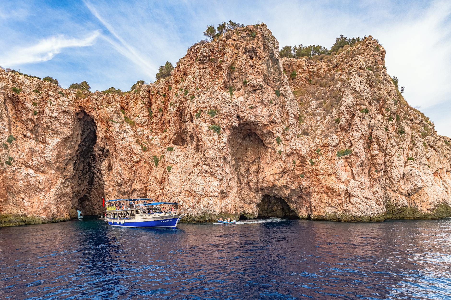 Small tour boat sailing past tall rocky cliffs and sea caves on the coast