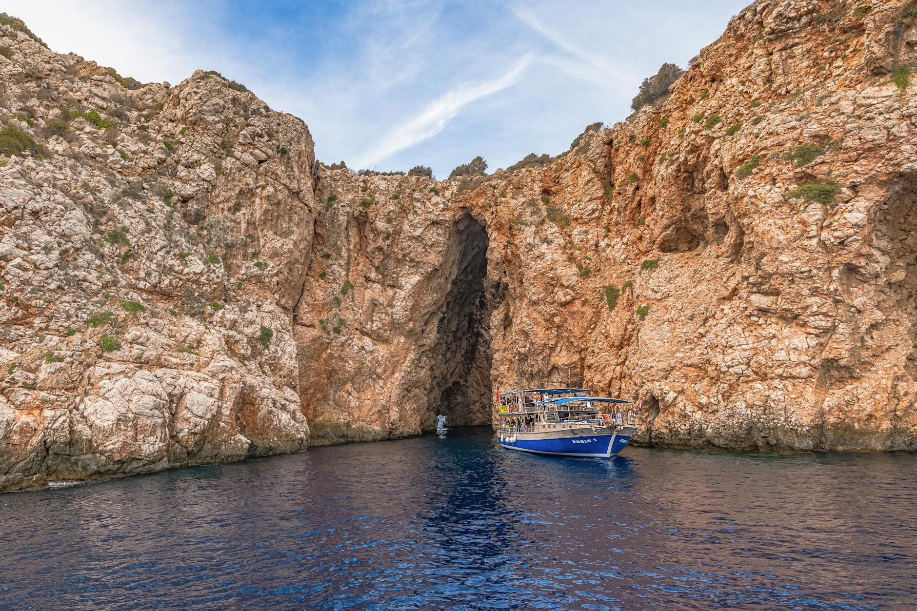 Tour boat heading toward a rocky cave entrance along a cliffy Mediterranean coastline