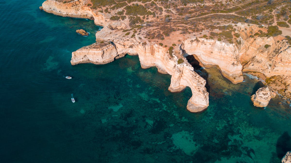 Aerial view of boats and cliff formations along the blue Algarve coastline