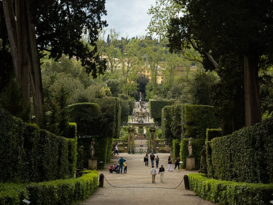 Visitors walking through a garden pathway lined with statues and tall hedges in Boboli Gardens Florence