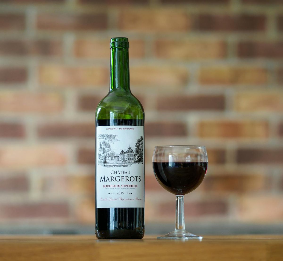 Bottle of Bordeaux red wine with a glass on a rustic wooden surface