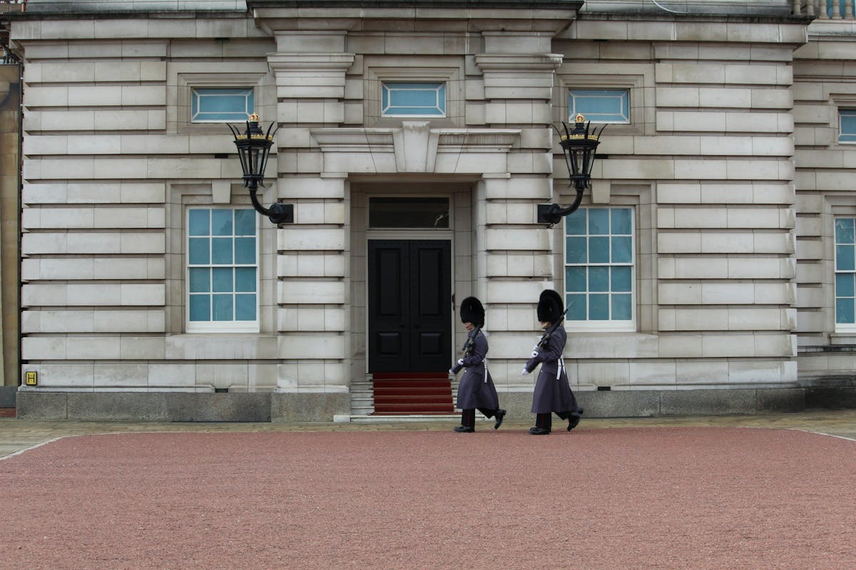Two guards in bearskin hats and red tunics marching at Buckingham Palace