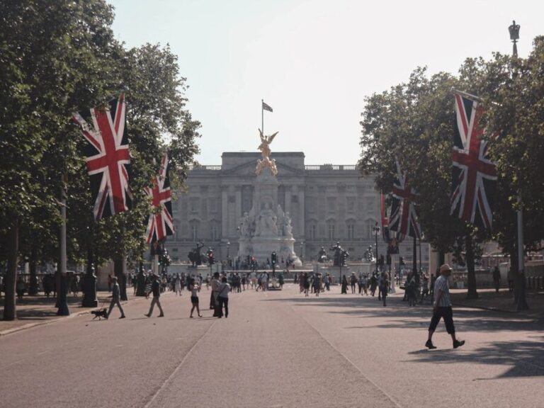 Buckingham Palace facade with Union Jack flags flying and tourists on the forecourt