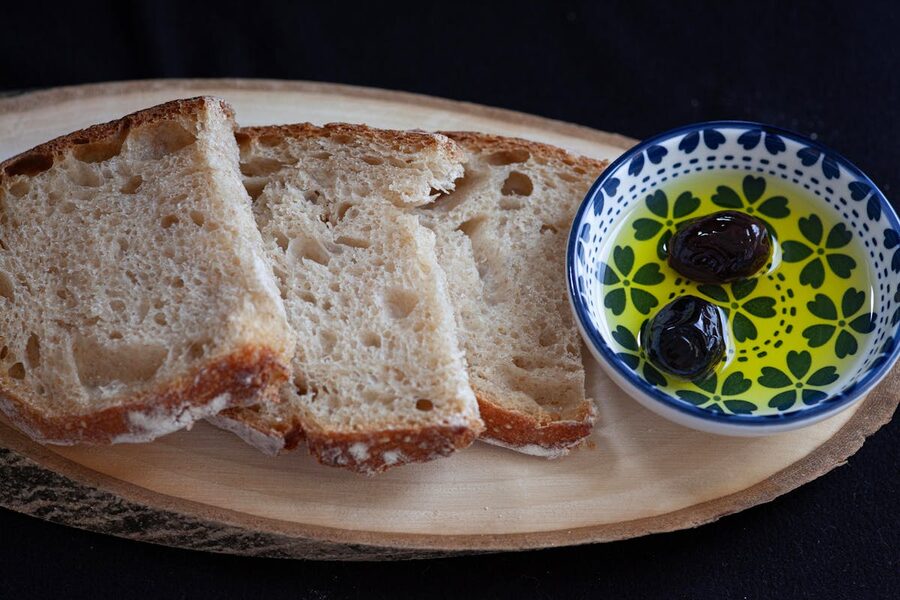 Sliced rustic bread served with a dish of olive oil and olives on a wooden board