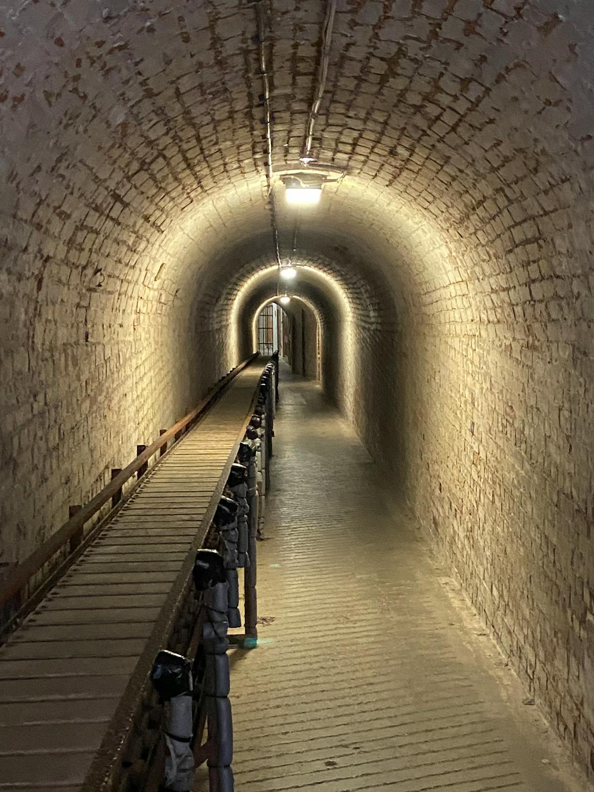Dimly lit brick tunnel with wooden walkway in an underground passage