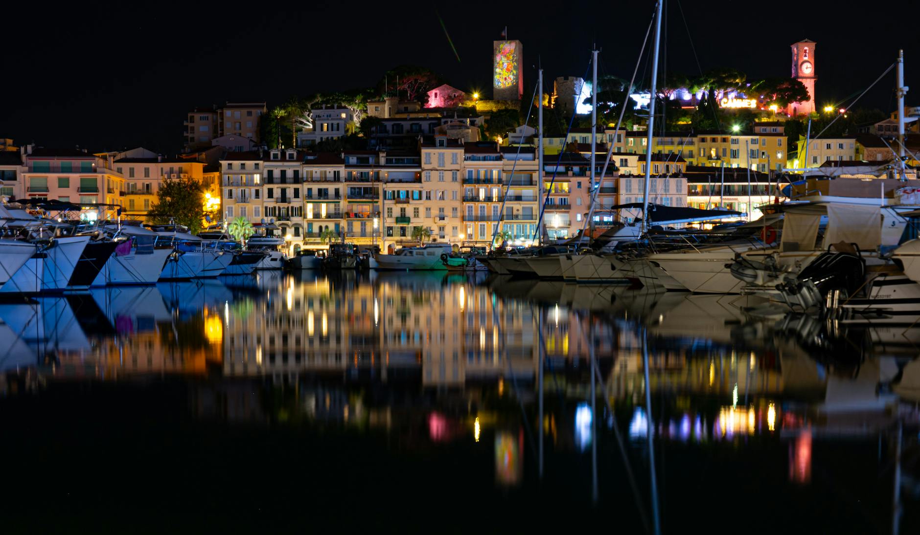 Cannes harbor at night with lights reflecting on calm water and boats moored