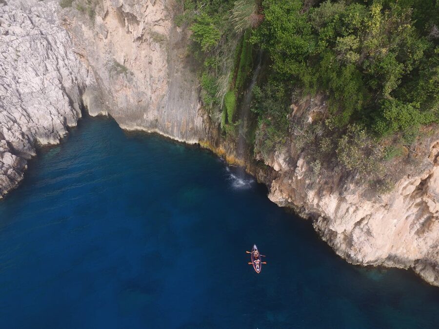Small boat floating in a sheltered turquoise cove next to steep coastal cliffs