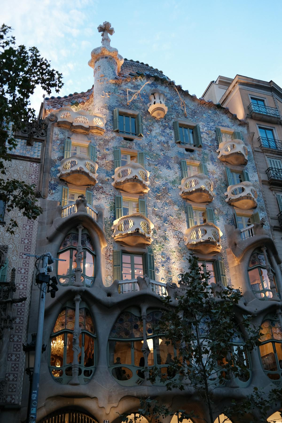The distinctive organic architecture of Casa Batllo with its coloured tile roof and cross-topped tower visible against the sky