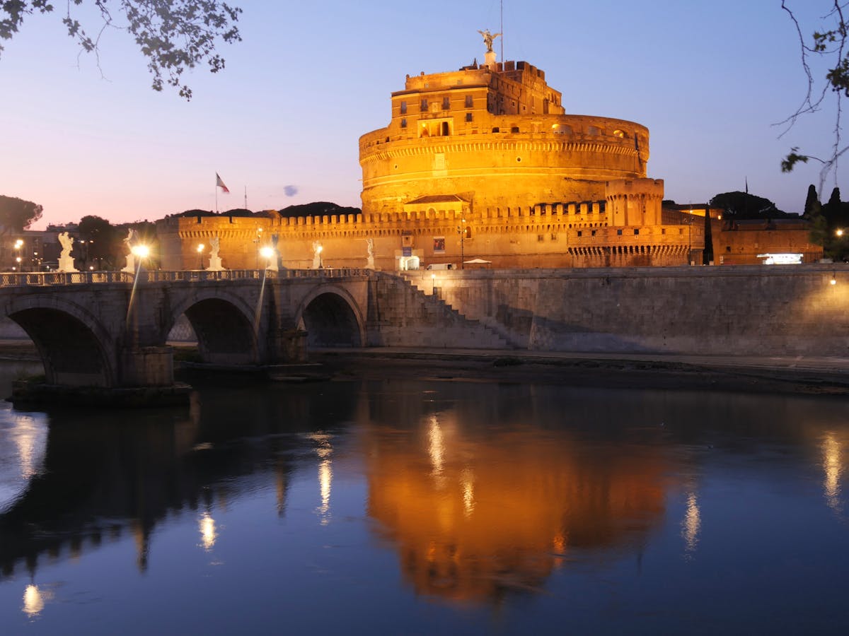 Castel Sant'Angelo lit up at sunset with reflections on the Tiber River