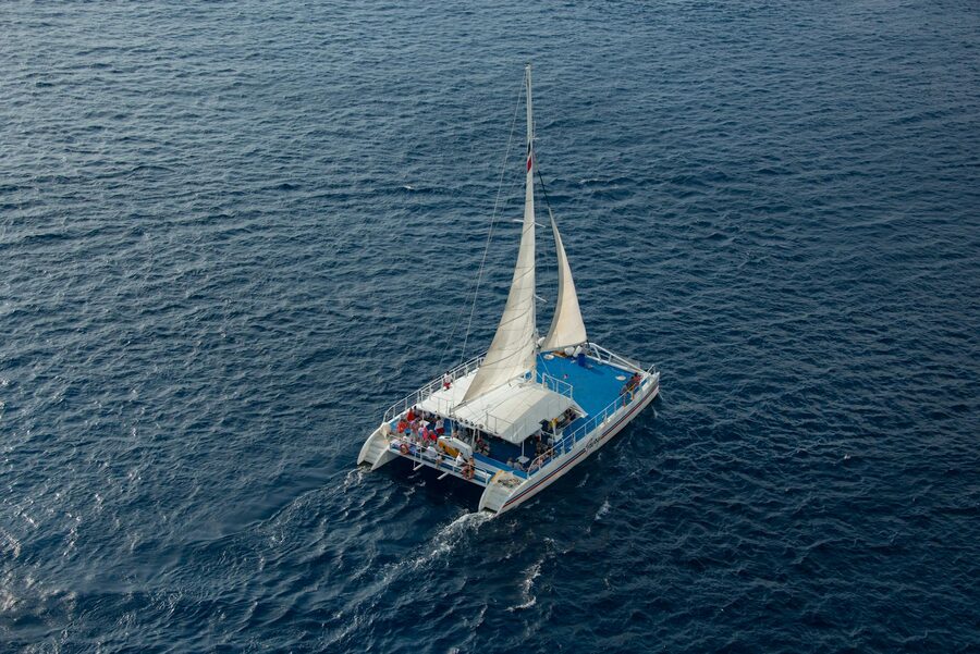 Aerial shot of a catamaran sailing with passengers on a clear blue sea