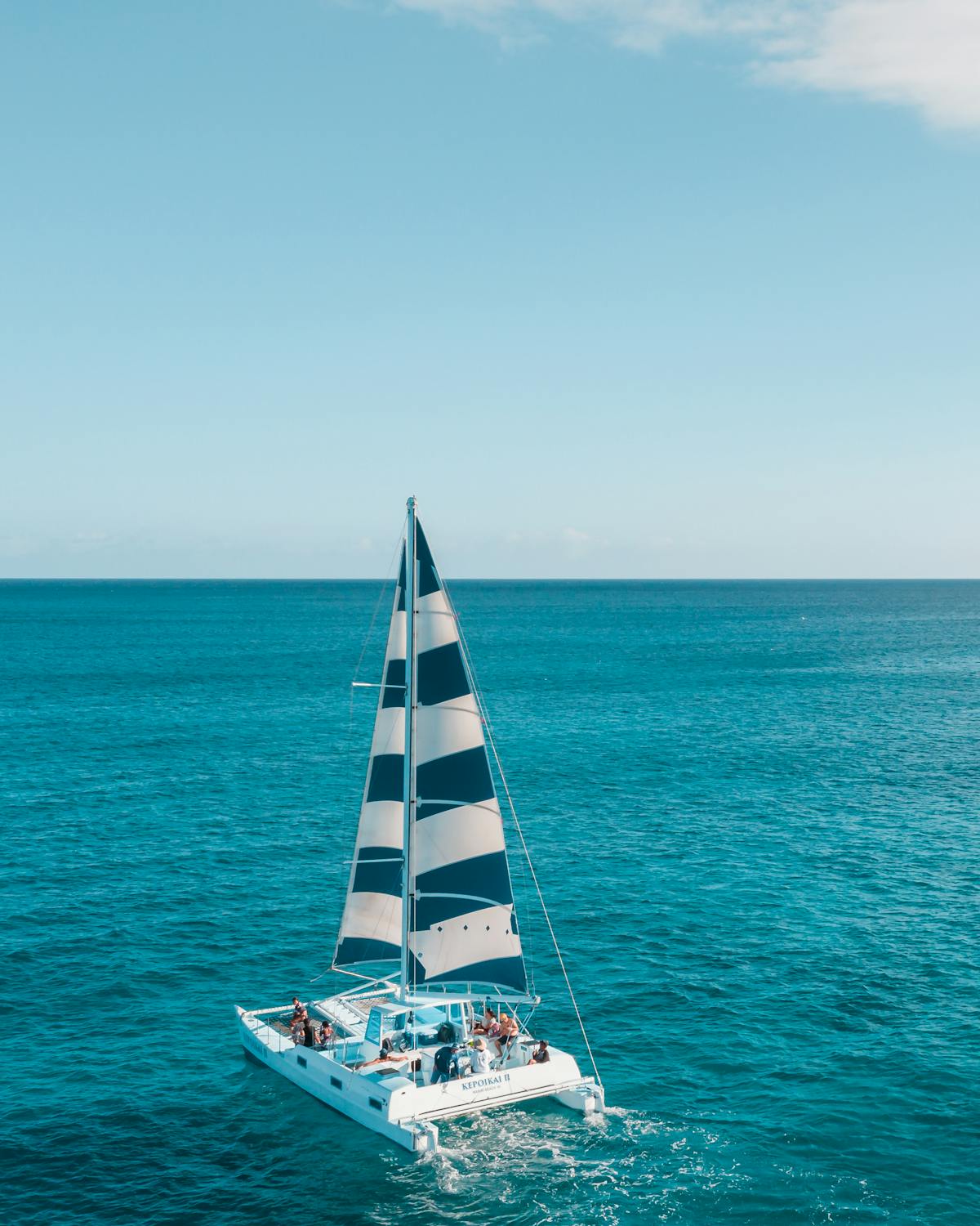 A catamaran with passengers sailing across calm blue ocean waters
