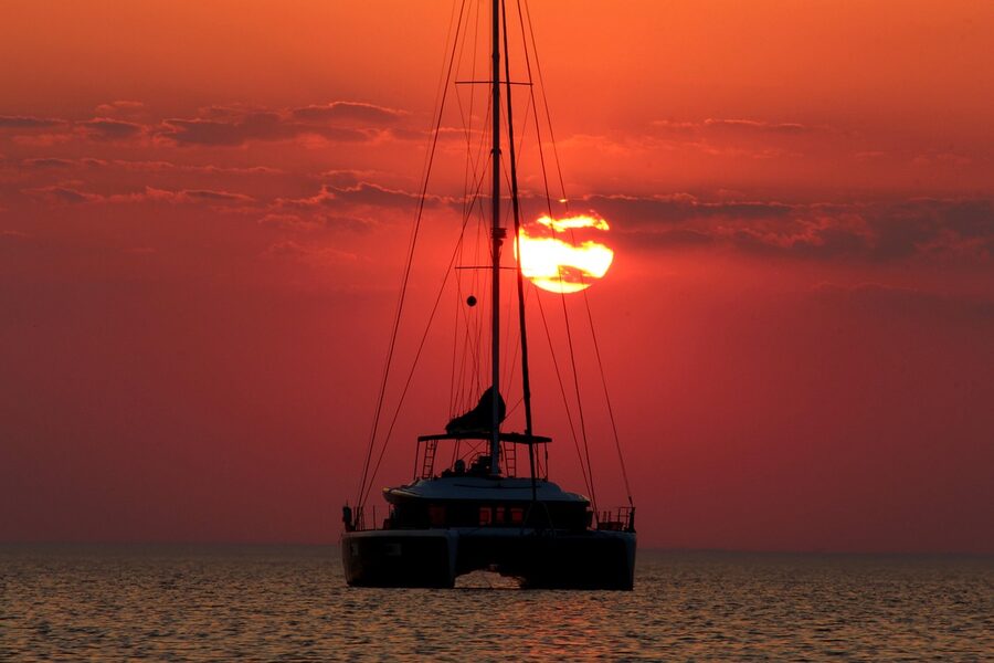 Catamaran sailing at dusk with orange sunset sky