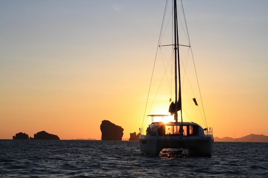 Catamaran yacht sailing on calm water at sunset