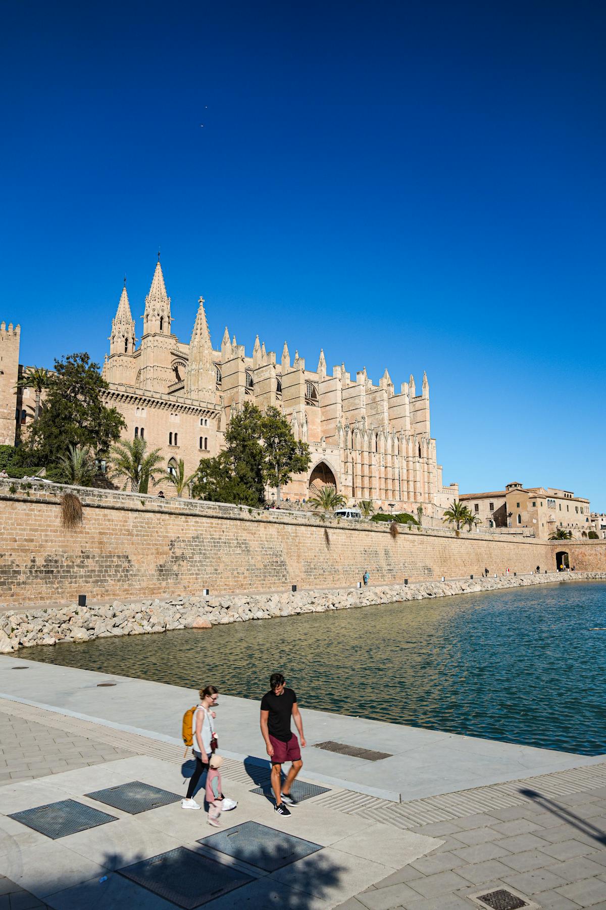 A couple walks along the waterfront promenade with Palma Cathedral in the background on a sunny day in Mallorca