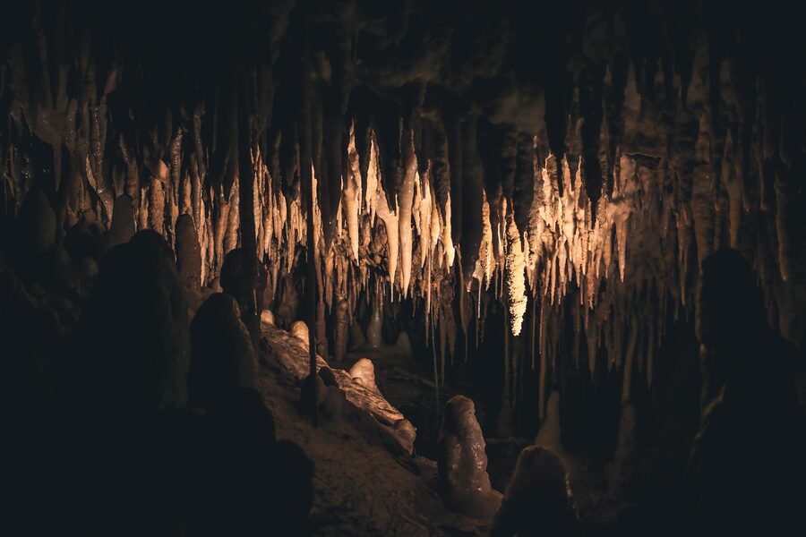 Underground cave chamber with illuminated stalagmites and stalactites reflected in still water