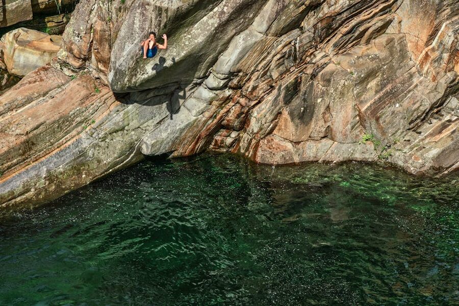 Person jumping off rocky cliff into green water