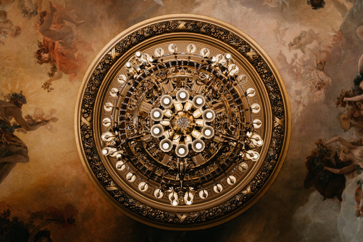 Intricate chandelier shining on a decorated ceiling in the Paris Opera House