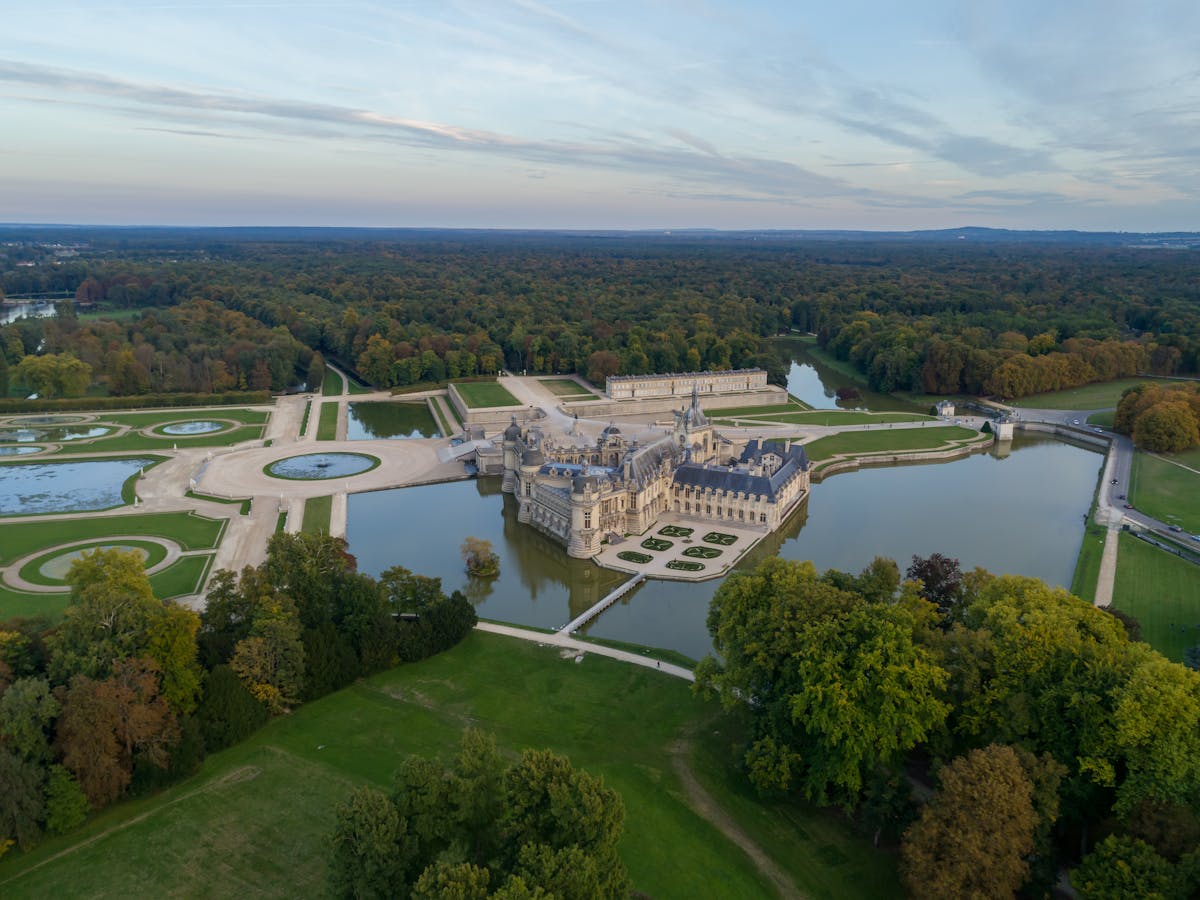 Aerial shot of Chateau de Chantilly surrounded by formal gardens and water features