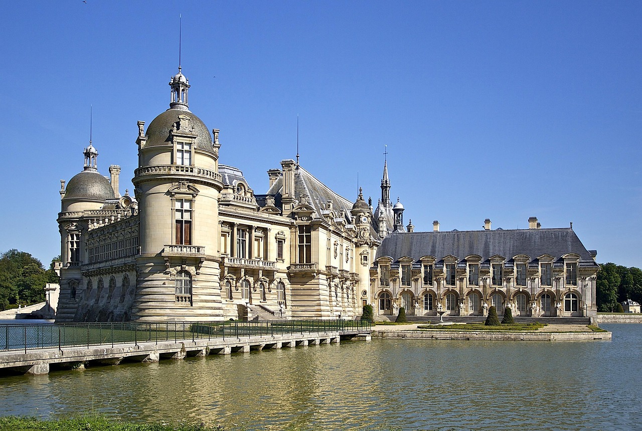 Chateau de Chantilly castle on lake with blue sky reflections