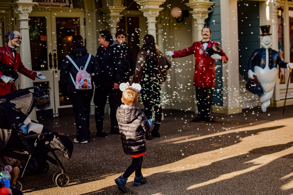 A child wearing Mickey Mouse ears enjoying bubbles at the park entrance