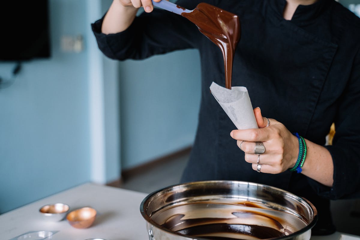 Chef pouring melted chocolate into a piping bag in a workshop