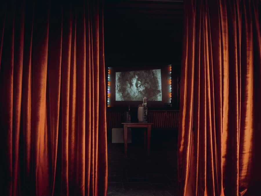 A cinema screening room with red curtains and classic film projector setup