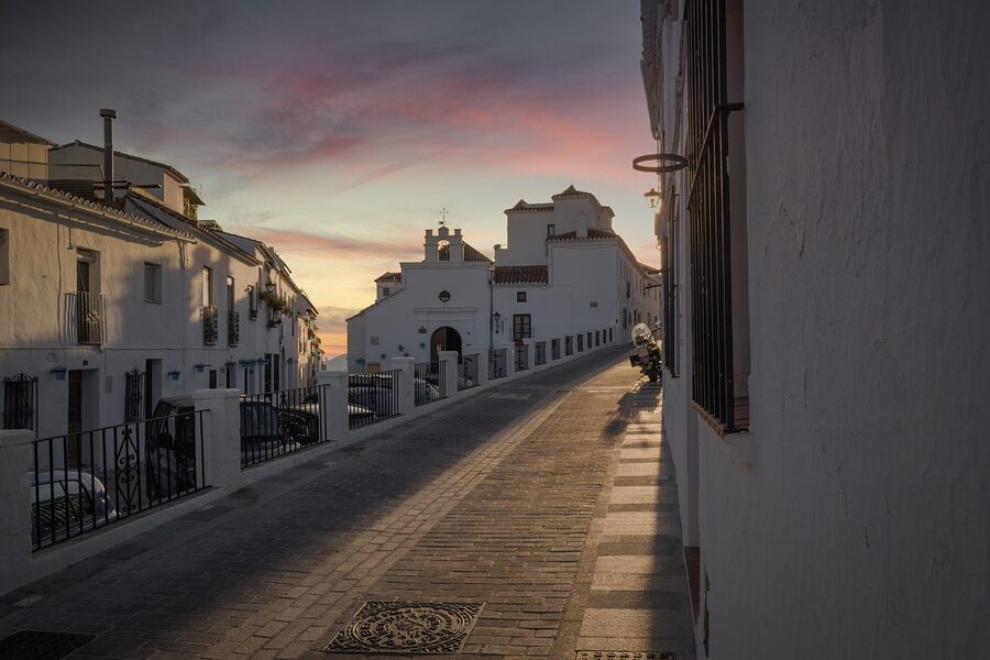 Narrow cobblestone alley with white buildings and sunset in Mijas Andalusia