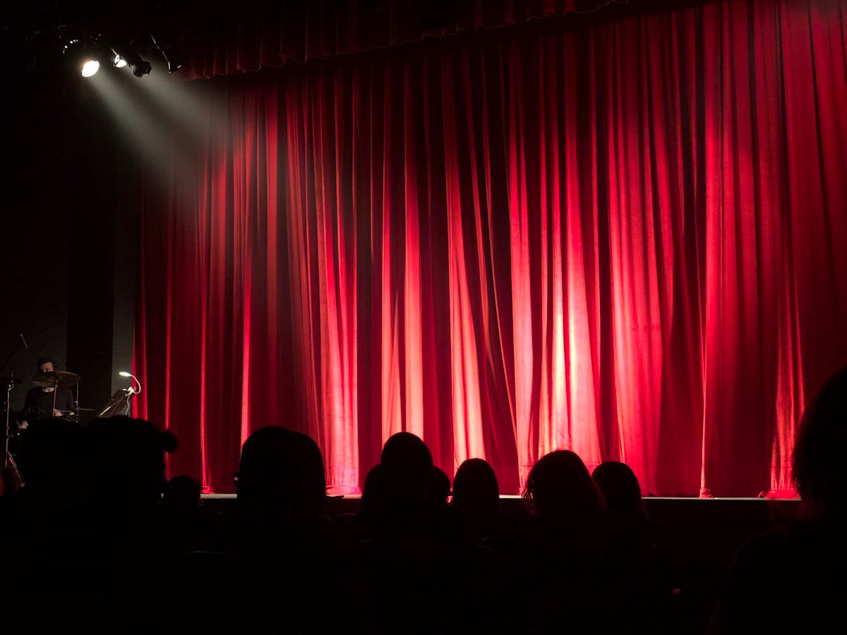 Dimly lit theater stage with red curtains and audience