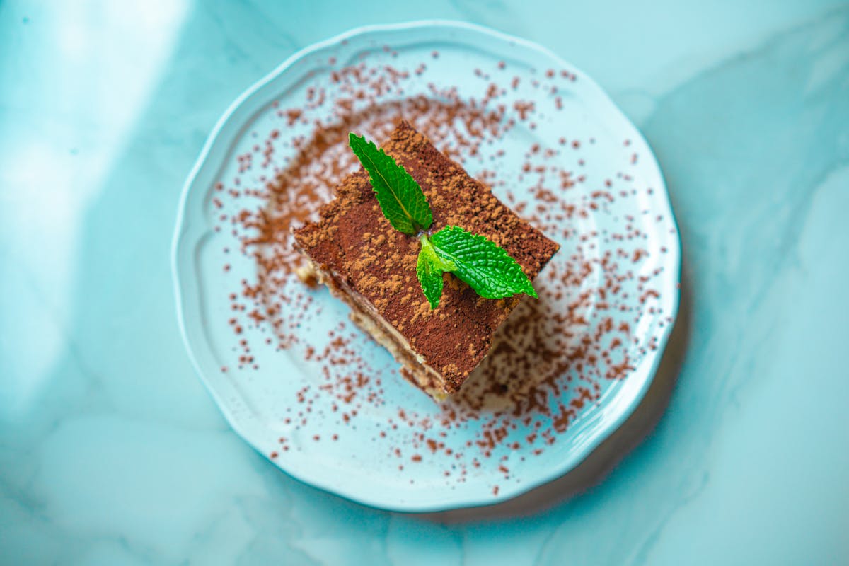Slice of tiramisu garnished with fresh mint on a marble plate
