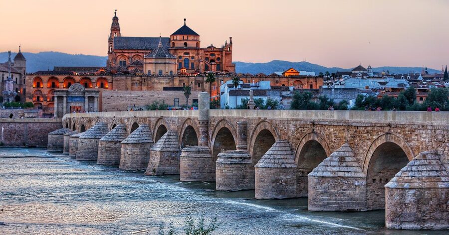 Roman Bridge in Cordoba illuminated in the evening with the Mezquita behind