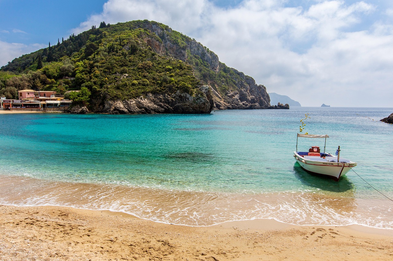 A small boat on the shore of a Corfu beach with turquoise water and green hillside