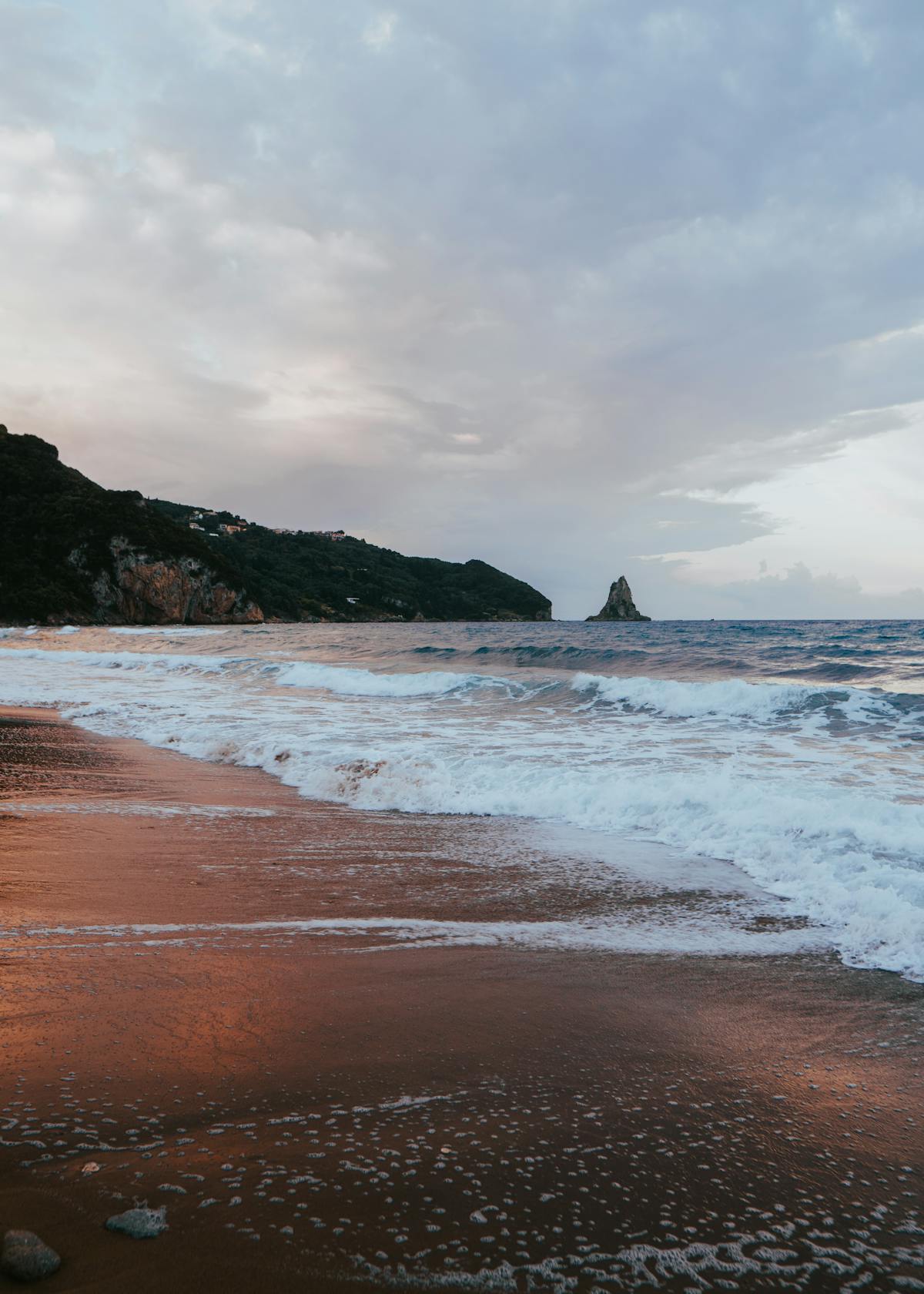 Sunset view of Corfu beach with dramatic cliffs and calm sea