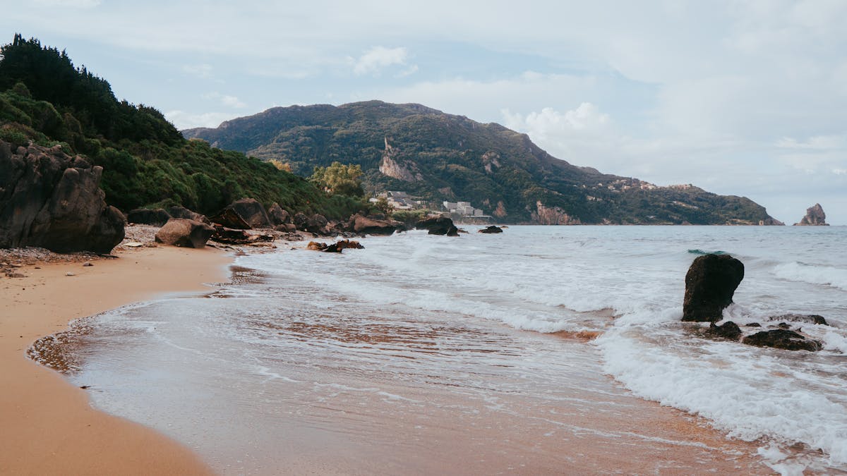 Waves breaking on a rocky Corfu coastline with lush green vegetation covering the cliffs