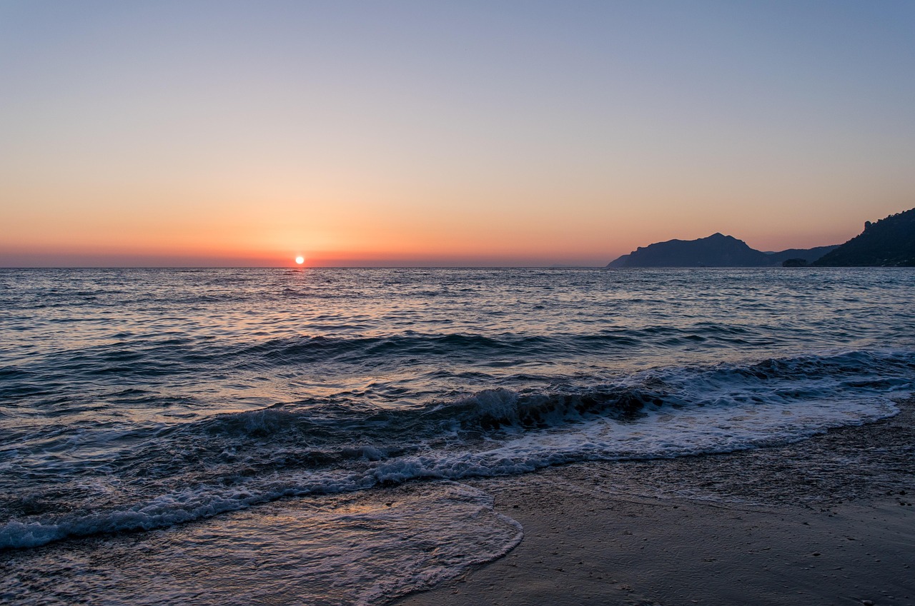 Boats silhouetted against a golden sunset over the Corfu coastline