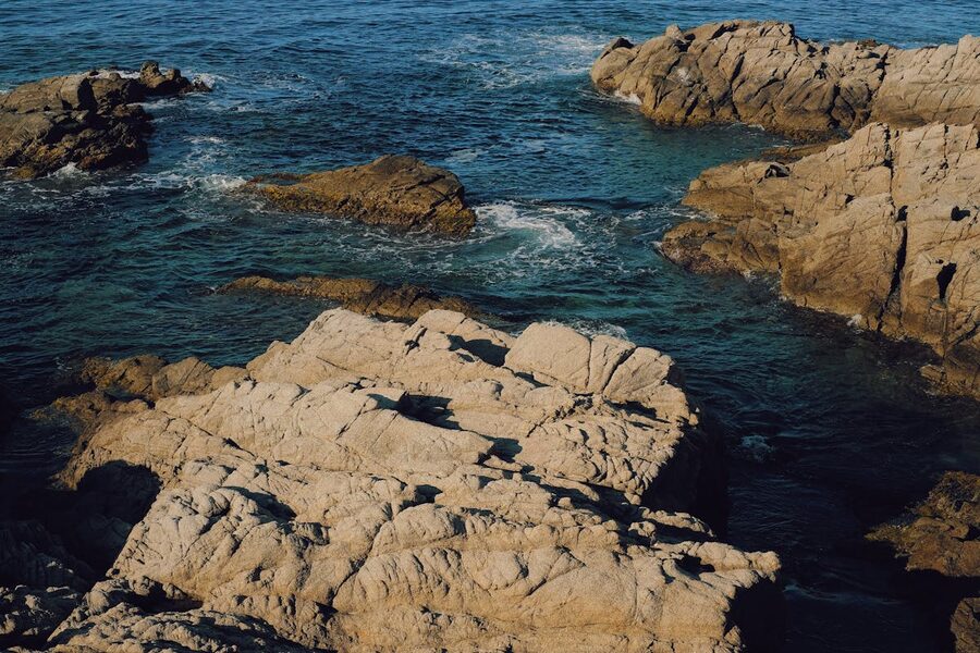Wide panoramic view of the rocky Costa Brava coastline with clear blue water and windswept vegetation