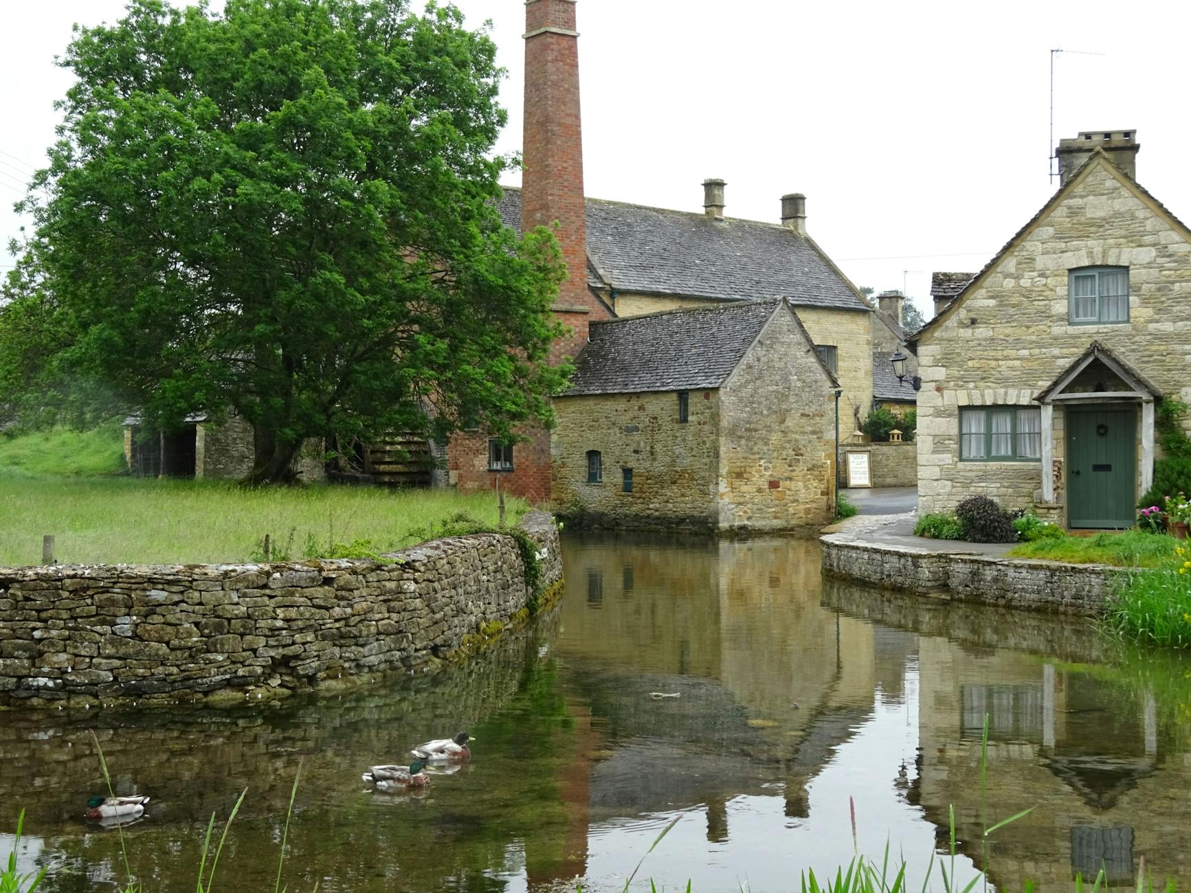 Historic stone mill building reflected in a calm pond in the Cotswolds