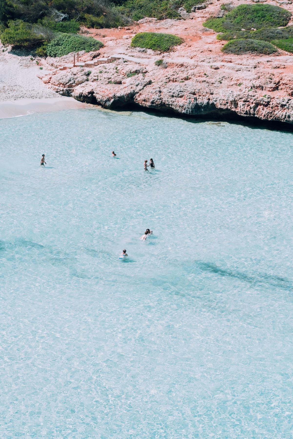 Aerial view of a tranquil Mediterranean cove with people swimming in clear turquoise waters