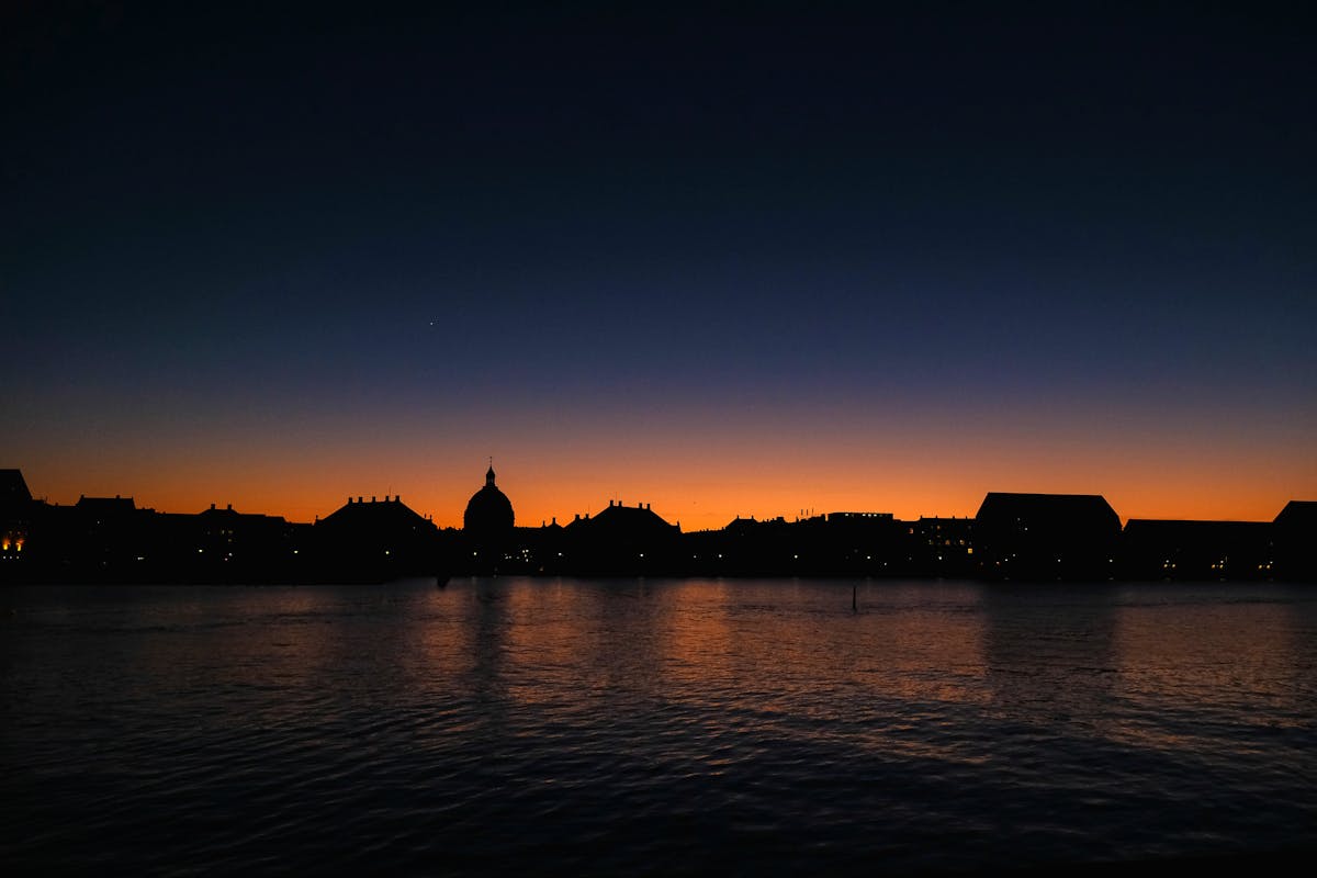 Silhouette of Copenhagen skyline against sunset reflecting on water