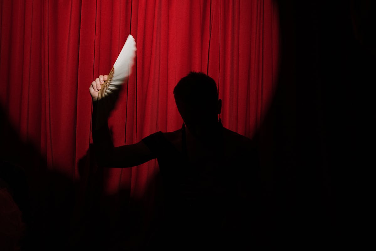 Silhouetted performer holding a fan against a red curtain backdrop