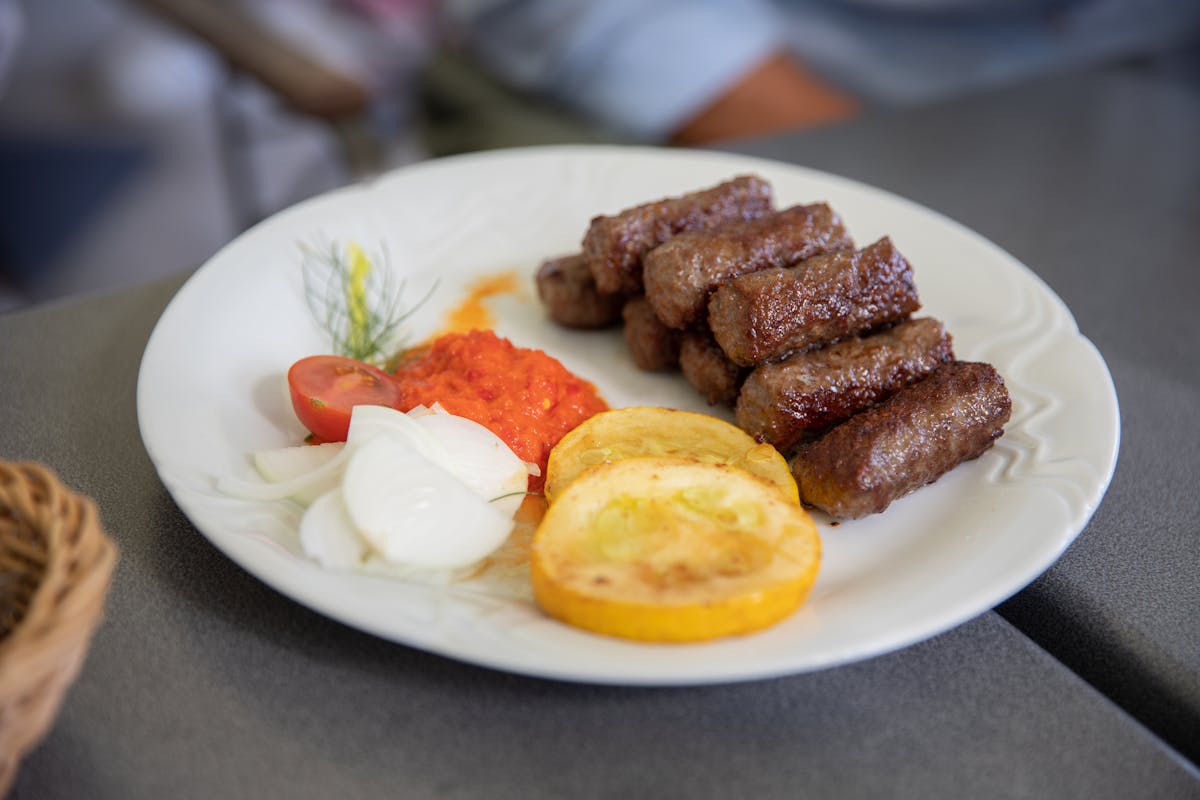 Plate of grilled cevapi with fresh vegetables and red pepper sauce