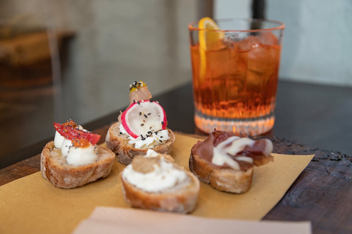 Plate of Italian crostini appetizers next to an Aperol Spritz cocktail