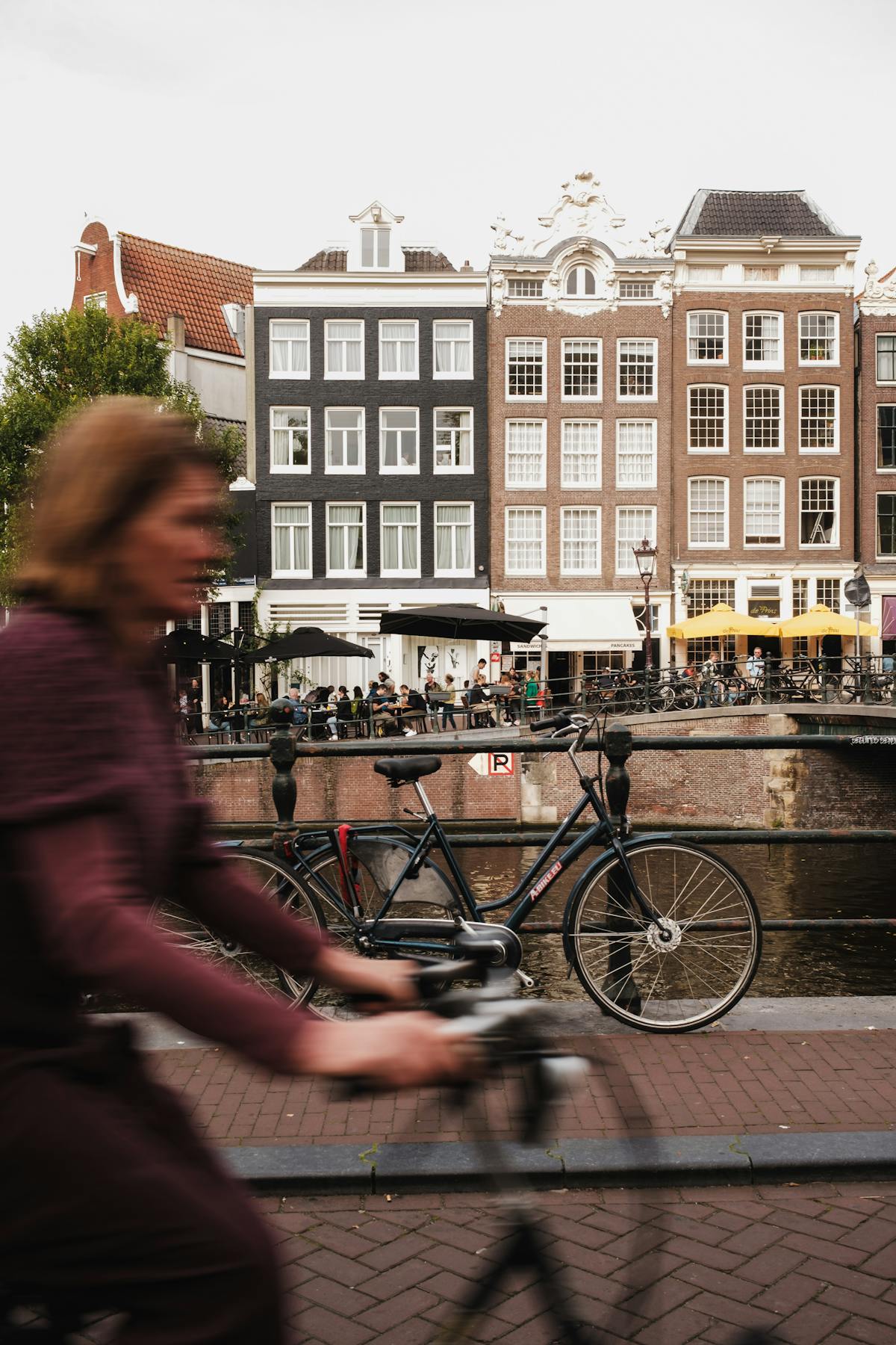 Woman cycling along canal with historic buildings in Amsterdam