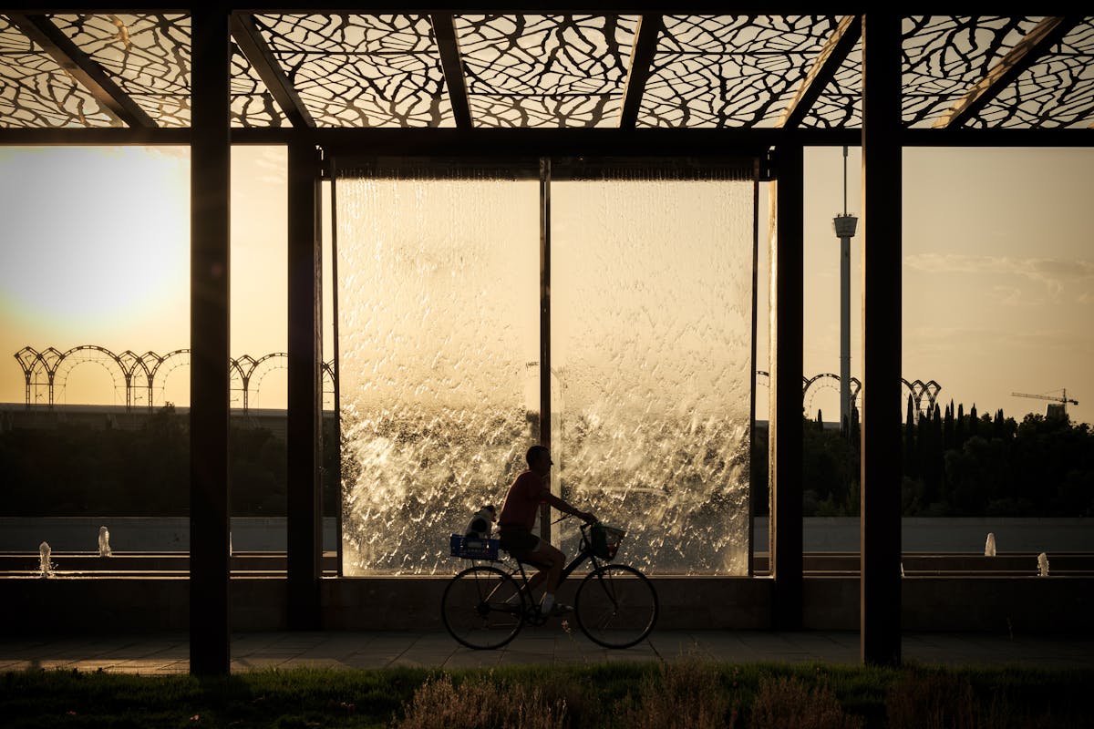 A cyclist rides past a modern waterfall structure at sunset in Seville Spain