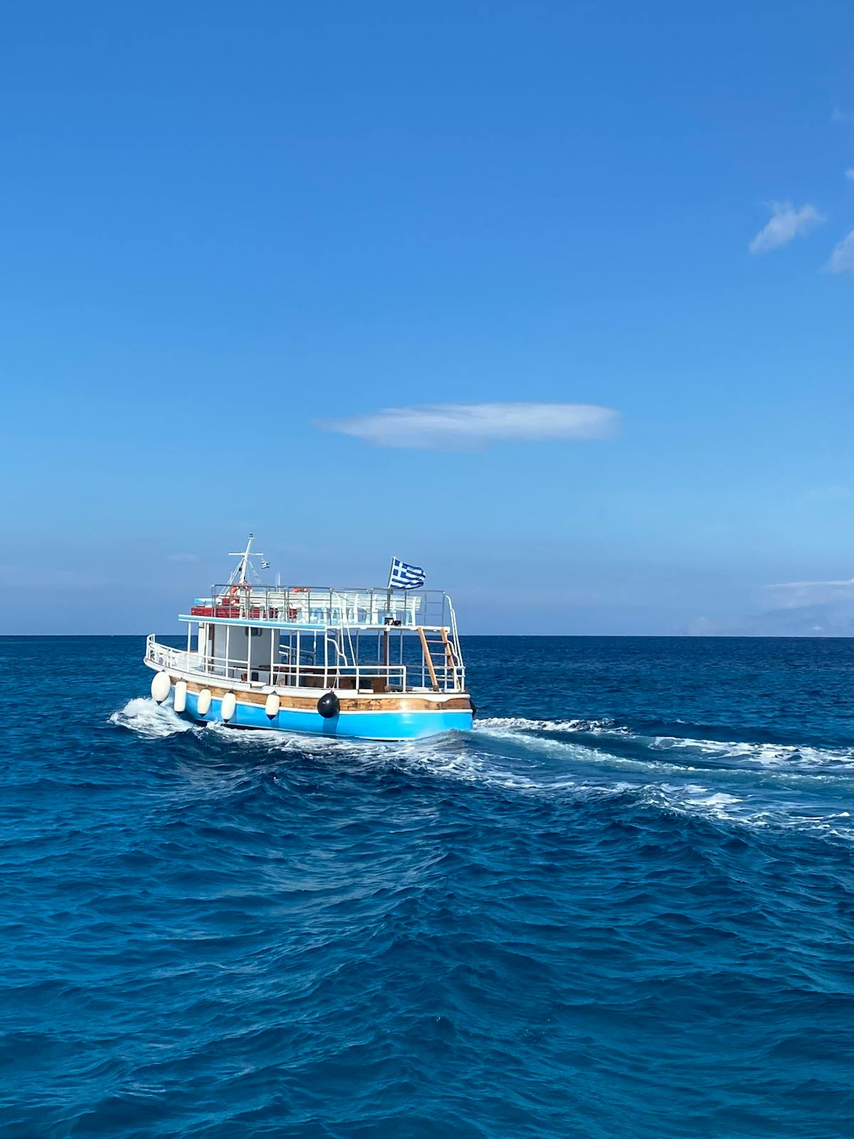 Boat with Greek flag sailing on the bright blue Aegean Sea