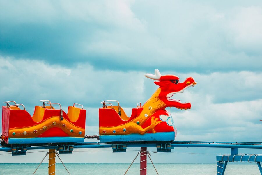 Colorful dragon-themed roller coaster against a cloudy sky at an amusement park