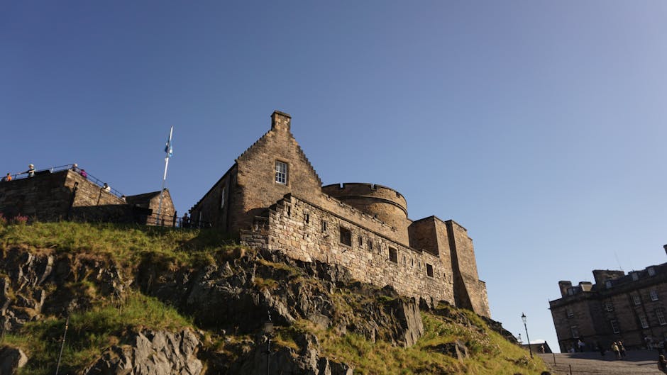 Edinburgh Castle on its rocky hill under a clear blue sky with green trees below