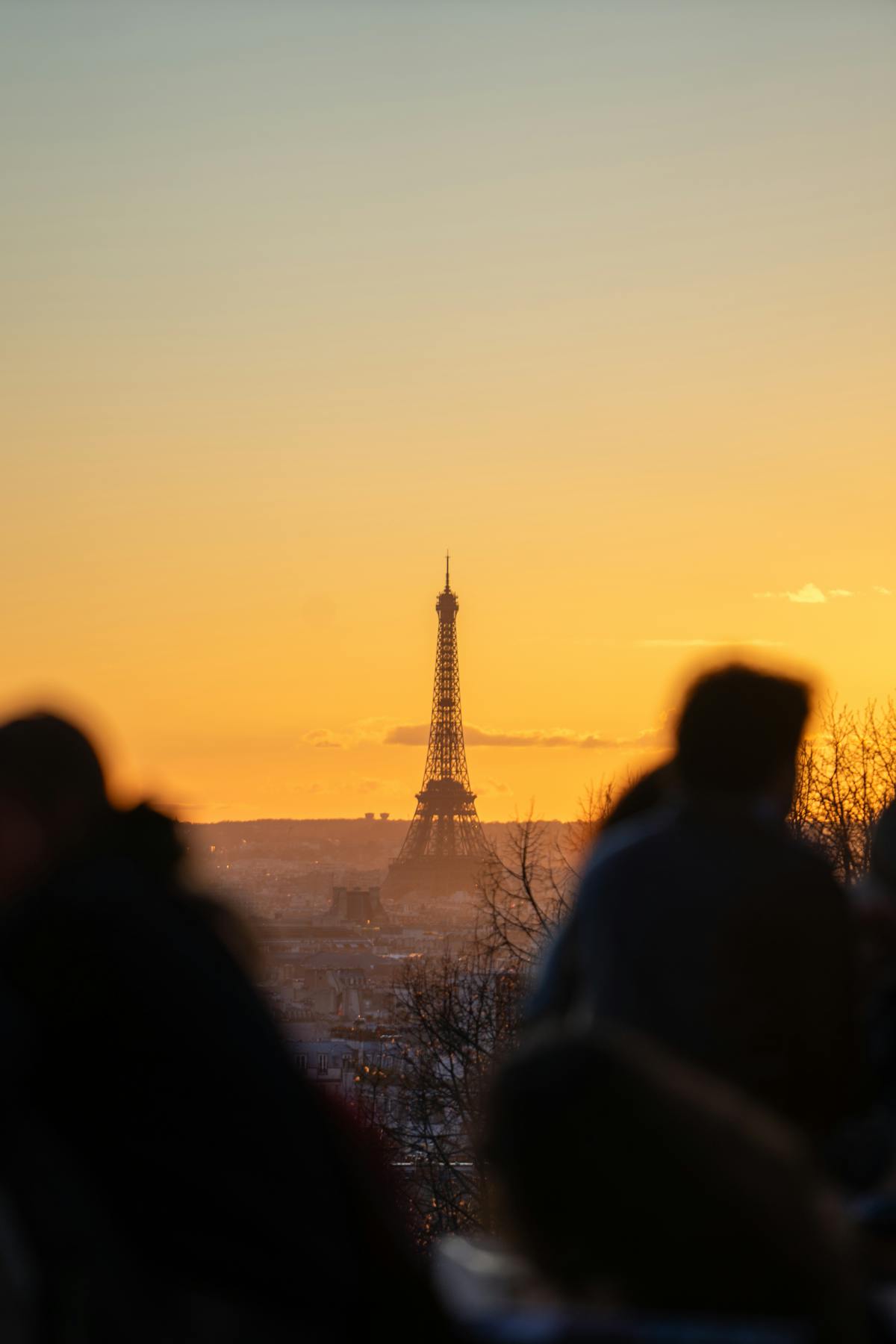 The Eiffel Tower in the distance against a fiery sunset with people watching from a hilltop