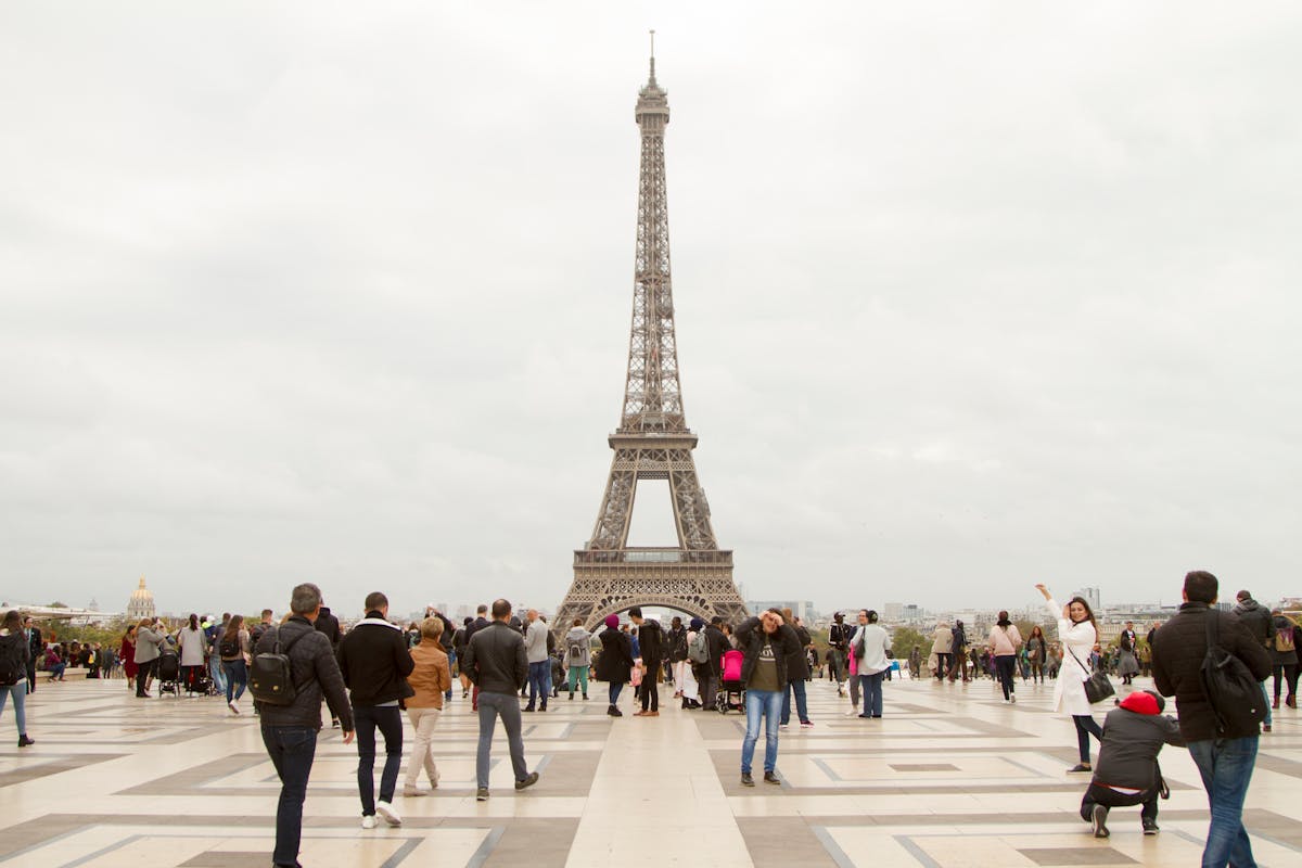 A crowd of visitors beneath the Eiffel Tower on an overcast Paris afternoon