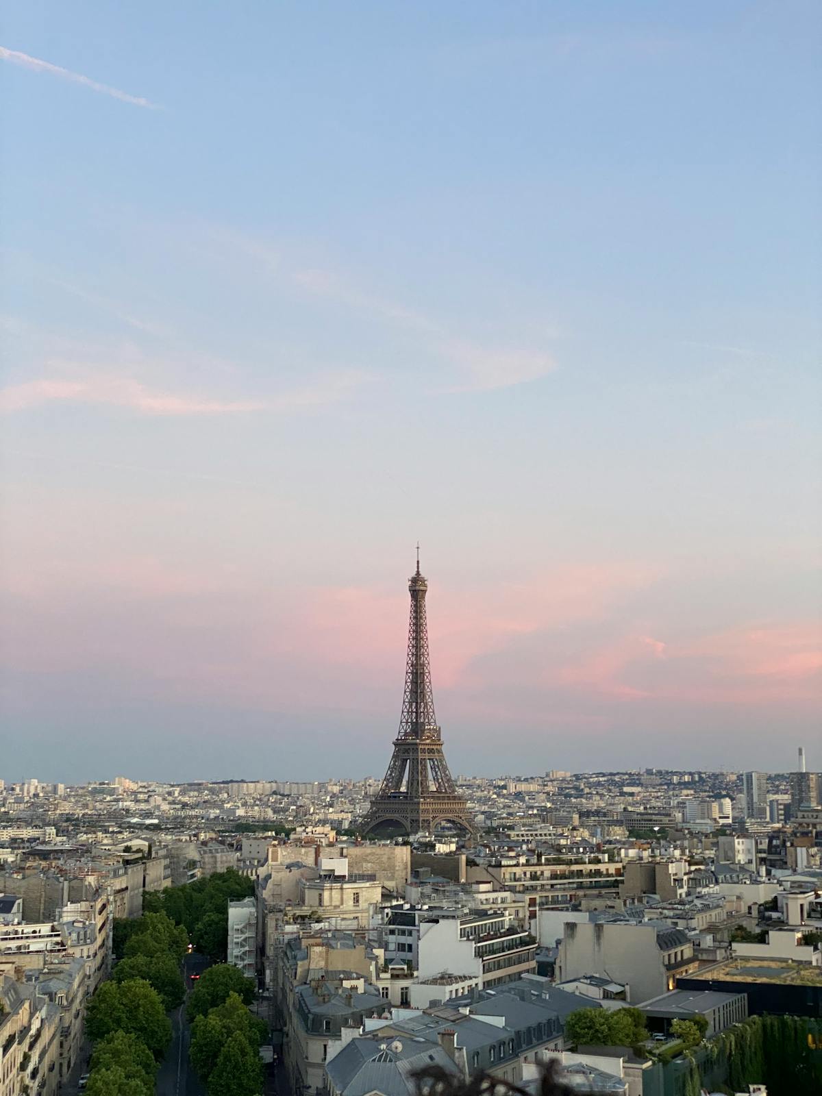 The Eiffel Tower silhouetted against a pastel pink and orange sunset sky